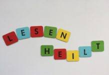 Steht doch da! Photoausstellung im Nachbarschaftsheim Kreuzberg LESEN HEILT! - SYMBOLBILD, zusammengesetzt aus 2mal 5 Buchstabenplättchen, schwarze Blockschrift auf roten, blauen, gelben und grünen Papplättchen. DA MAN DIESEN TEXT liest, heilt er womöglich sofort (instantly). Lesen und dann länger leben, das stimmt garantiert. - Beitragsbild für Steht doch da!, die Photoausstellung zum Analphabetismus und dessen Wirkung in der Gesellschaft, Benachteiligung, auf die aufmerksam gemacht werden soll, um sie zu verringern und irgendwann verschwinden zu lassen.