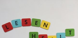 Steht doch da! Photoausstellung im Nachbarschaftsheim Kreuzberg LESEN HEILT! - SYMBOLBILD, zusammengesetzt aus 2mal 5 Buchstabenplättchen, schwarze Blockschrift auf roten, blauen, gelben und grünen Papplättchen. DA MAN DIESEN TEXT liest, heilt er womöglich sofort (instantly). Lesen und dann länger leben, das stimmt garantiert. - Beitragsbild für Steht doch da!, die Photoausstellung zum Analphabetismus und dessen Wirkung in der Gesellschaft, Benachteiligung, auf die aufmerksam gemacht werden soll, um sie zu verringern und irgendwann verschwinden zu lassen.