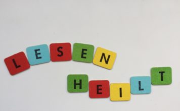 Steht doch da! Photoausstellung im Nachbarschaftsheim Kreuzberg LESEN HEILT! - SYMBOLBILD, zusammengesetzt aus 2mal 5 Buchstabenplättchen, schwarze Blockschrift auf roten, blauen, gelben und grünen Papplättchen. DA MAN DIESEN TEXT liest, heilt er womöglich sofort (instantly). Lesen und dann länger leben, das stimmt garantiert. - Beitragsbild für Steht doch da!, die Photoausstellung zum Analphabetismus und dessen Wirkung in der Gesellschaft, Benachteiligung, auf die aufmerksam gemacht werden soll, um sie zu verringern und irgendwann verschwinden zu lassen.