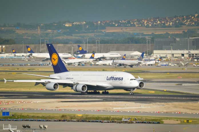 Ein Flughafen mit mindestens 8 Flugzeugen am Boden, darunter 7 von der deutschen Lufthansa AG. Es ist Tag und die Sonne scheint. Im Hintergrund sieht man auf dem sanft ansteigenden Gelände rechts einen Ort mit einer Kirche. Flughafenstreik am 1.2.2024