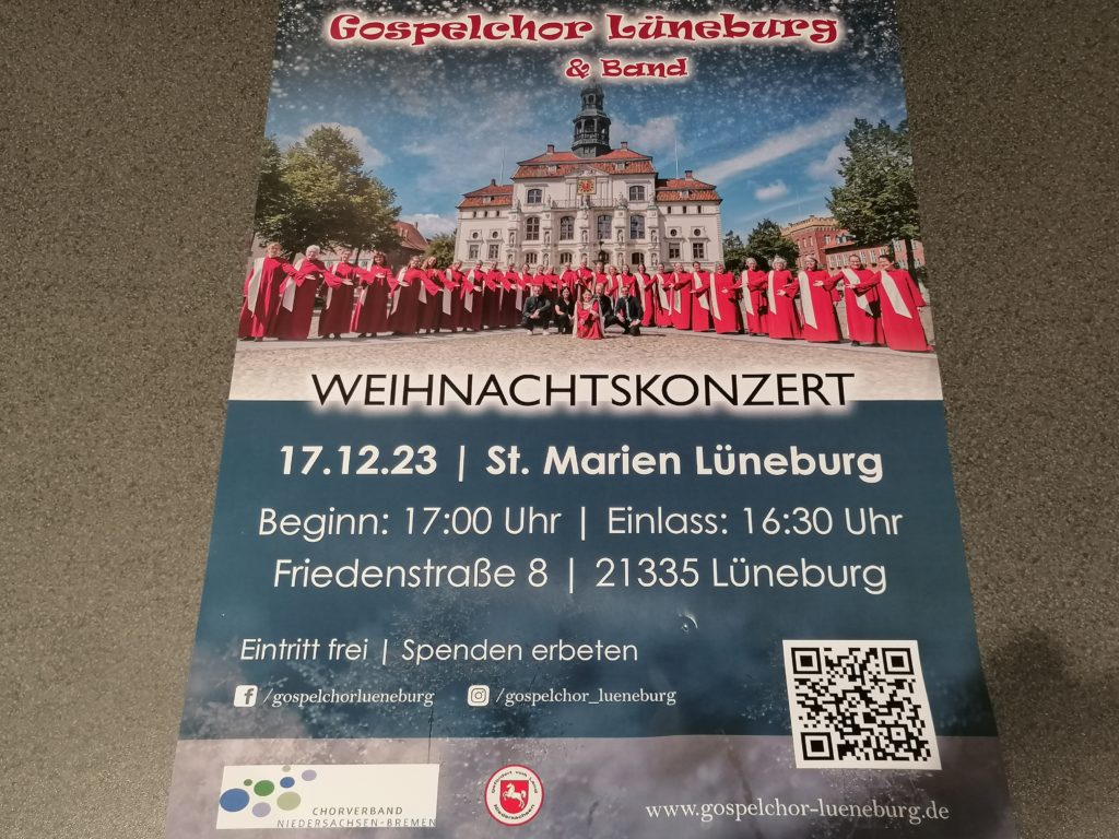 Plakat, auf Tisch liegend, Das Weihnachtskonzert des Gospelchors Lüneburg mit Band findet am 17.12.23 um 17 Uhr in der Marienkirche Friedenstraße 8 statt.